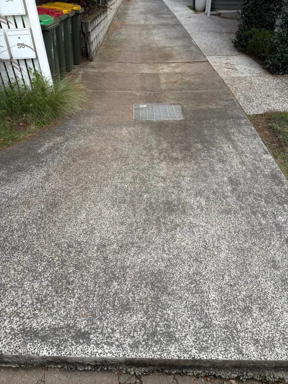 Concrete driveway cleaned in the foreground, dirty grey concrete still visible further back.