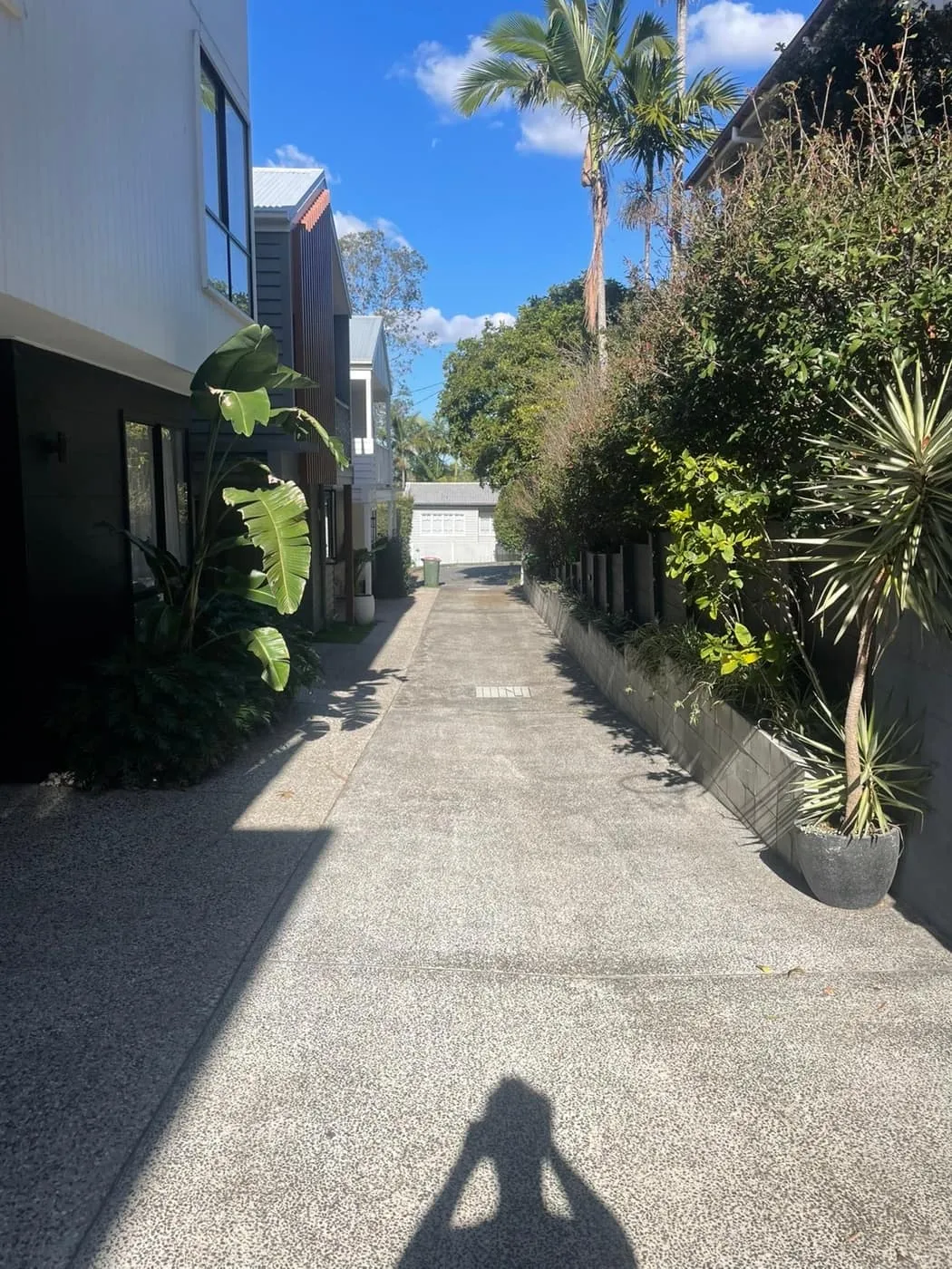 Long exposed-aggregate driveway between townhouses, freshly cleaned on a sunny Brisbane day.